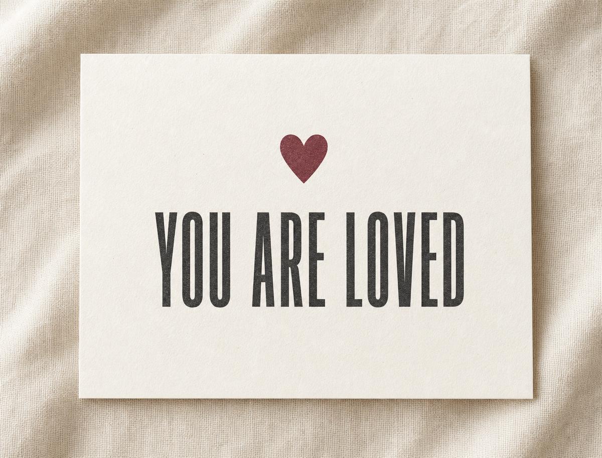 Encouragement card printed with a burgundy heart above the words "You are loved" on warm off-white paper